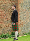Man wearing a traditional Scottish kilt standing against a stone wall.