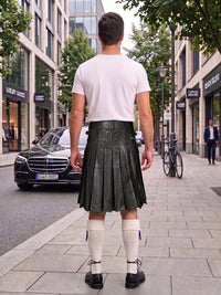 A man viewed from behind wearing a white t-shirt, a dark green pleated leather kilt, white knee-high socks, and black shoes, standing on a city sidewalk.