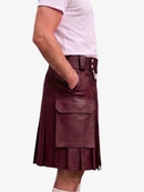 A dark green faux-leather kilt with pleated detailing, a front flap pocket, and a belt with silver-tone buttons, shown on a model wearing a light pink t-shirt against a white background.