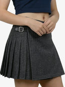 Person wearing a pleated gray skirt with a black top on a white background