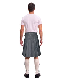 A man shown from the back wearing a gray pleated kilt, a light pink t-shirt, white knee-high socks, and black shoes, against a plain white background.