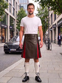 A man stands on a city sidewalk wearing a white crew-neck t-shirt and a dark brown leather kilt with red side panels, paired with white knee-high socks and black leather shoes.