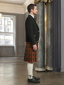 Man wearing a black jacket and red plaid kilt in an elegant interior setting.