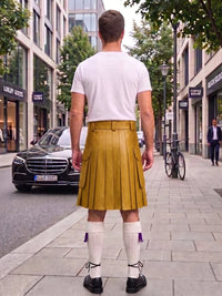 A man viewed from behind wearing a mustard yellow leather kilt, white t-shirt, white knee-high socks, and black shoes, standing on a city sidewalk.