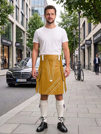 A man stands on a city sidewalk wearing a mustard yellow kilt with white geometric line patterns, a white t-shirt, white knee-high socks, and black shoes. The background shows a blurred street scene with buildings, a black Mercedes-Benz car, and a bicycle.