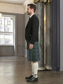 Man wearing a black jacket, plaid kilt, and white knee-high socks in an elegant room.