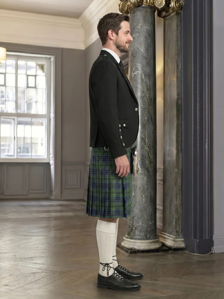 Man wearing a black jacket and green plaid kilt in an elegant interior setting.