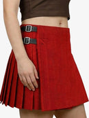 Red pleated skirt with black buckles worn by a person on a white background