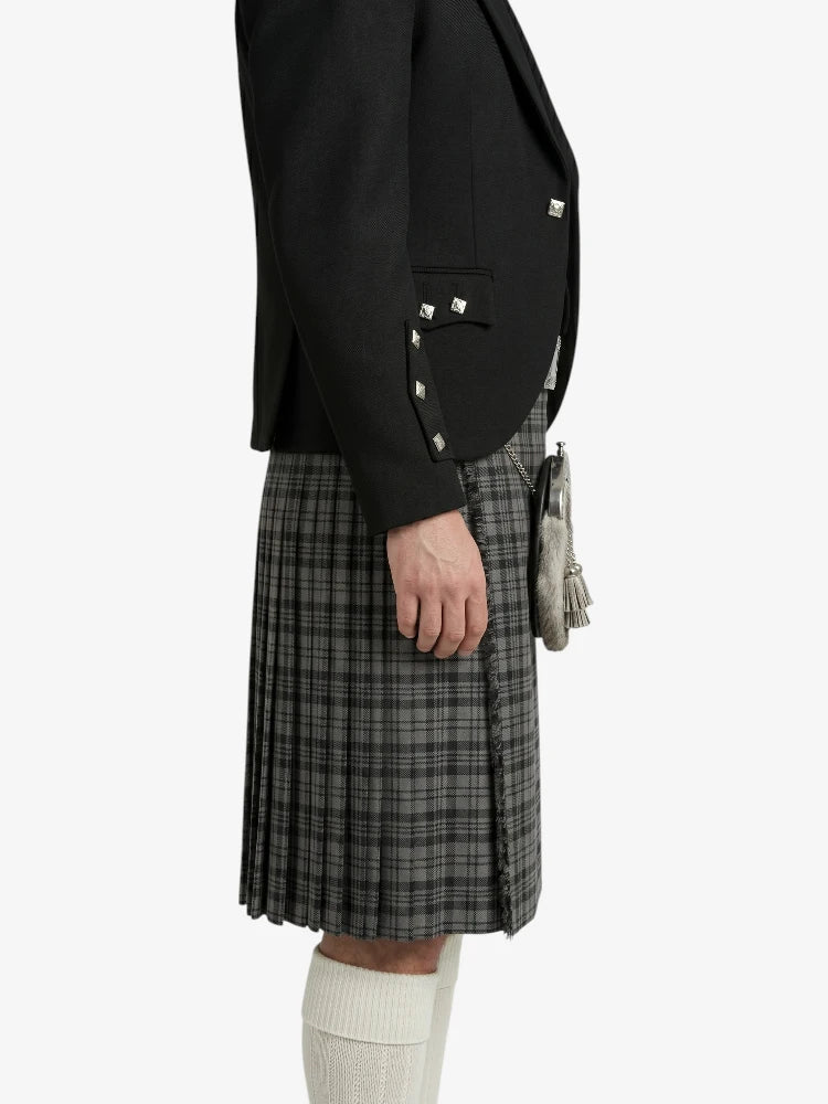 Person wearing a black blazer with studded details and a plaid skirt on a white background